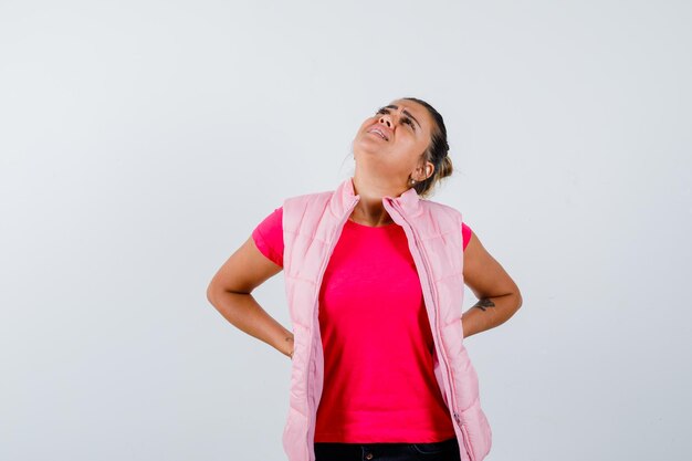 Mulher com dor nas costas vestindo camiseta, colete e parecendo cansada