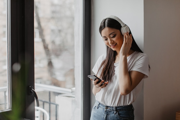 mulher com fones de ouvido brancos perto da janela