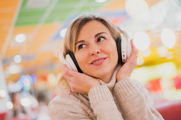 Mulher com fones de ouvido no pescoço, olhando para longe perto de luzes de Natal