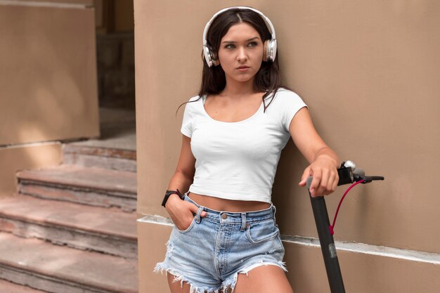 Mulher com fones de ouvido posando ao lado de uma scooter elétrica