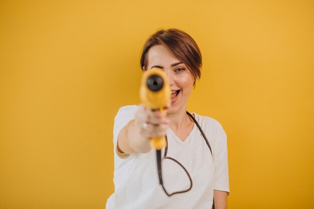 Mulher com furadeira elétrica em fundo amarelo