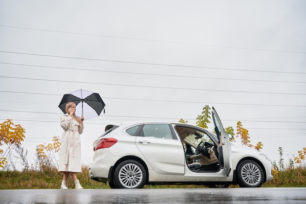 Foto grátis mulher com guarda-chuva em pé perto do carro e falando ao telefone