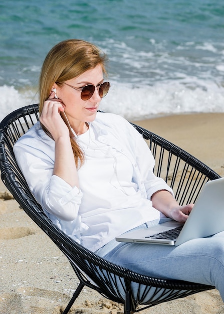 Mulher com laptop e óculos de sol, trabalhando na praia