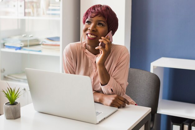 Mulher, com, laptop, falando telefone, em, escritório