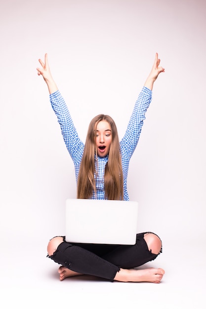 Foto grátis mulher com laptop vencendo com sucesso. comemorando a sessão de pernas cruzadas no chão - isolado na parede branca.