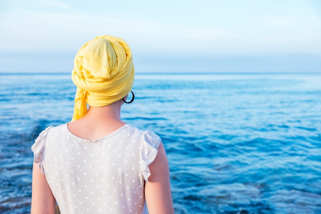 Mulher com lenço amarelo, apreciando a vista para o mar