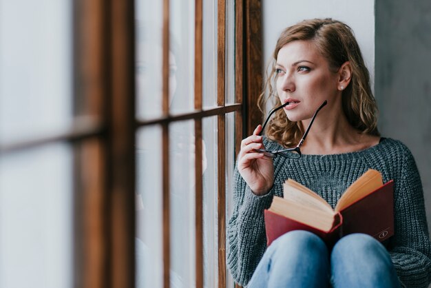 Mulher com livro e óculos pensando