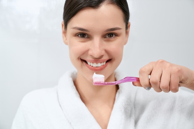 Mulher com manto branco depois do banho segurando uma escova de dentes