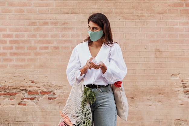 Mulher com máscara facial e sacolas de compras usando desinfetante para as mãos