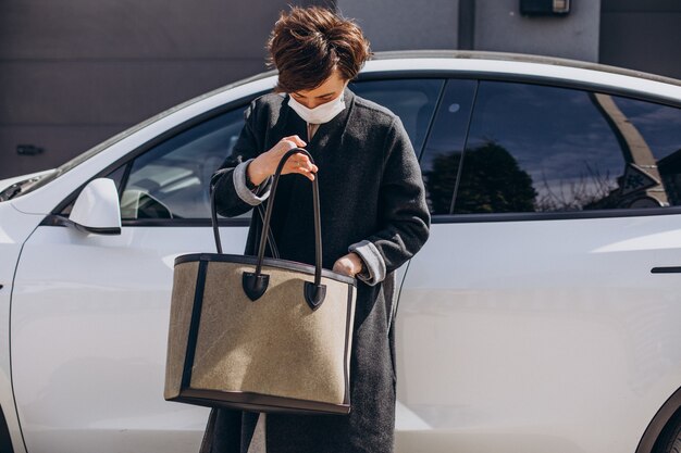 Mulher com máscara facial parada ao lado do carro