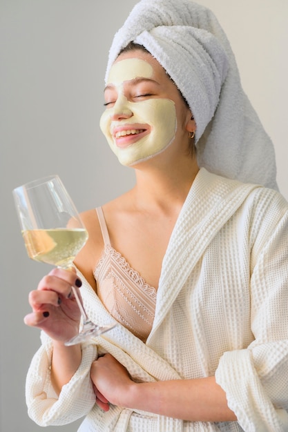 Mulher com máscara facial segurando copo de vinho