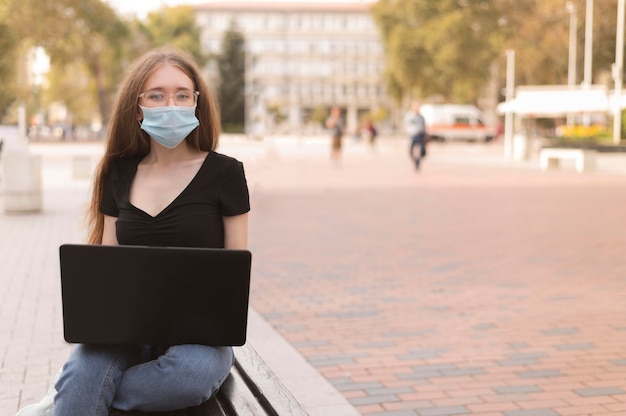 Foto grátis mulher com máscara facial trabalhando em um laptop do lado de fora