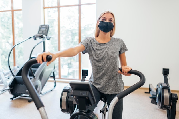 Mulher com máscara médica durante pandemia se exercitando na academia