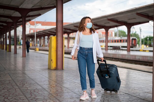 Mulher com máscara médica e bagagem na estação de trem pública