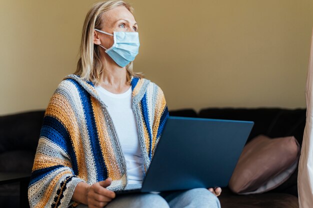 Mulher com máscara médica e laptop em quarentena em casa