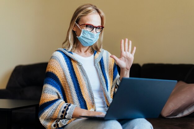 Mulher com máscara médica e laptop em quarentena