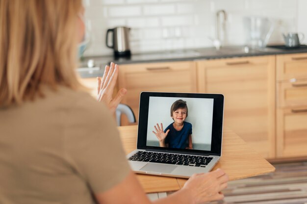 Mulher com máscara médica e sobrinho de videochamada de laptop durante quarentena