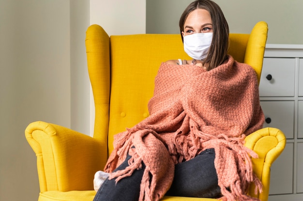 Foto grátis mulher com máscara médica em casa na poltrona durante a pandemia