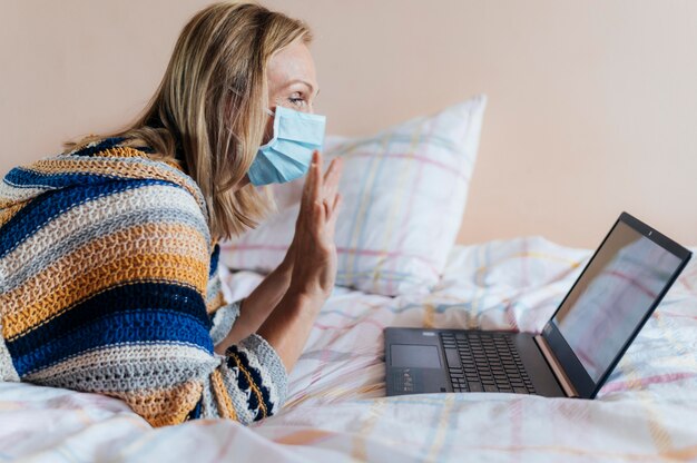 Mulher com máscara médica em quarentena em casa com laptop