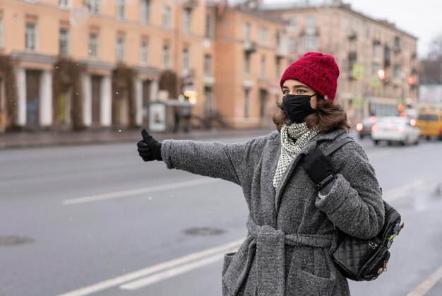Mulher com máscara médica pedindo carona na cidade