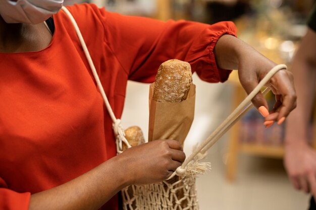 Mulher com máscara médica recebendo pão no supermercado