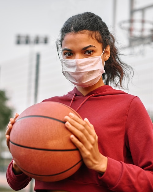 Mulher com máscara médica segurando uma bola de basquete