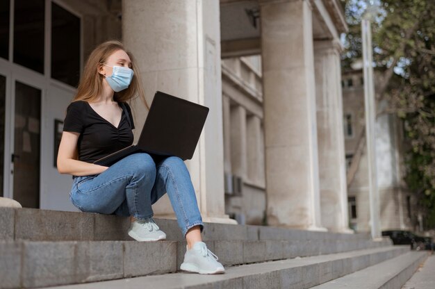 Mulher com máscara médica sentada na escada do lado de fora com espaço de cópia