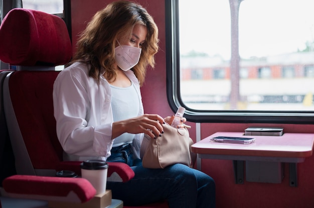 Mulher com máscara médica usando desinfetante para as mãos enquanto viaja de trem público