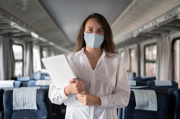 Mulher com máscara médica viajando de trem público e usando laptop