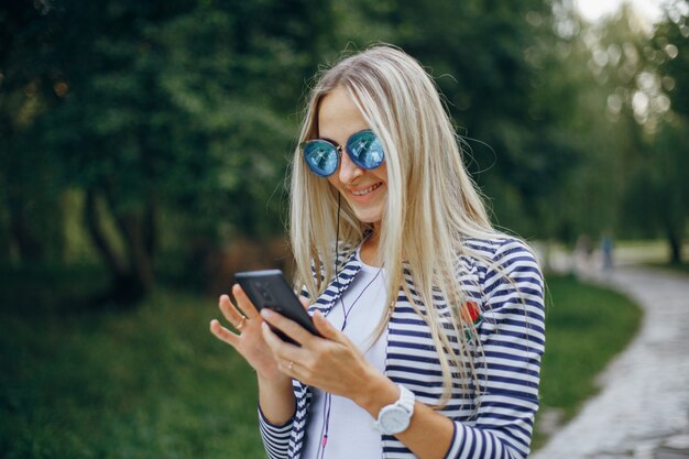 Mulher com óculos de sol de sorriso que datilografa em um celular