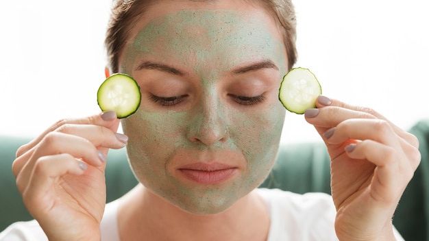 Mulher com os olhos fechados, aplicando fatias de pepino