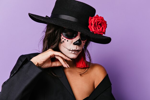 Mulher com os olhos fechados toca suavemente o rosto pintado. Fotografia de menina em roupas pretas com detalhes vermelhos.