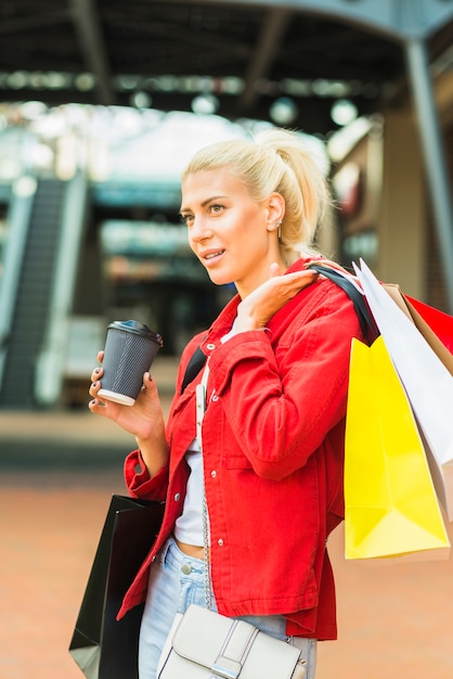 Mulher com pacotes de compras e copo de bebida