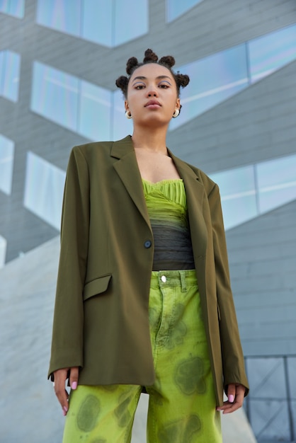 Foto grátis mulher com penteado na moda maquiagem brilhante vestida com roupas da moda posa contra uma parede cinza do lado de fora