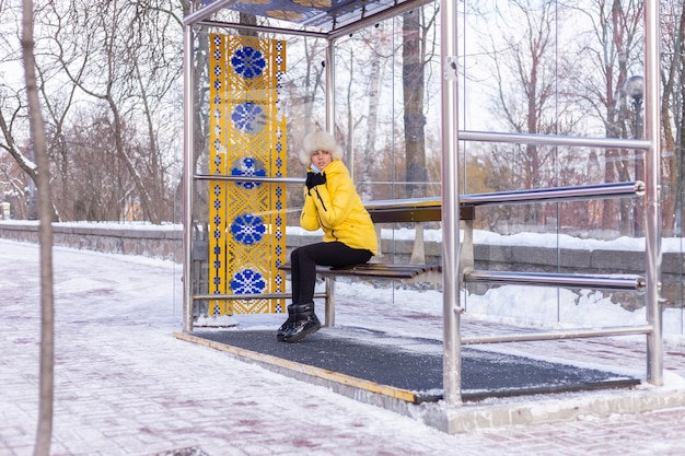 Mulher com roupas de inverno em um dia frio esperando um ônibus em um ponto de ônibus