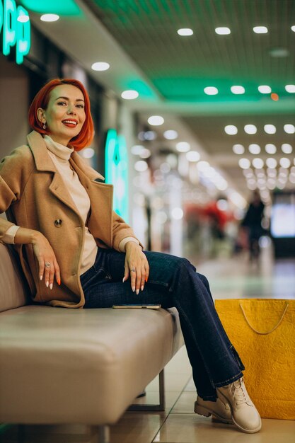 Mulher com sacolas de compras sentada na carruagem em shopping center