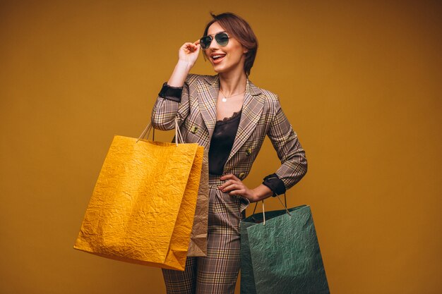 Mulher com sacos de compras no estúdio em fundo amarelo isolado