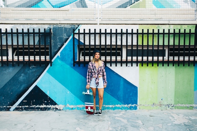 Mulher com skate na frente de uma parede