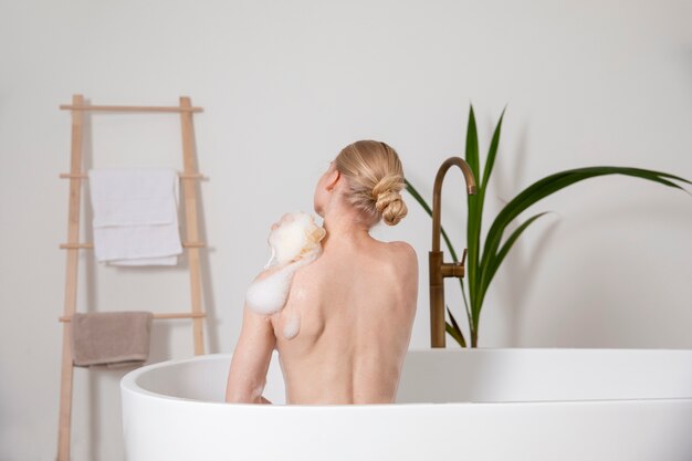 Mulher com tiro médio usando esponja de banho