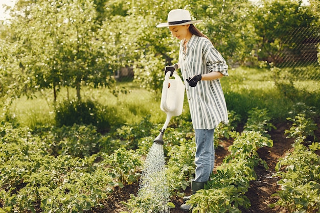 Mulher com um chapéu segurando um funil e trabalhando em um jardim