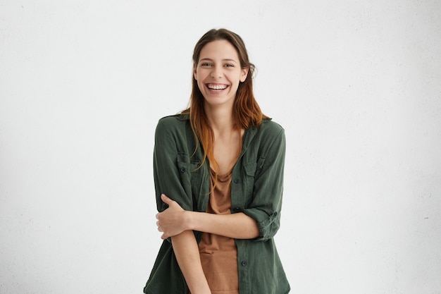 mulher com um largo sorriso vestida de jaqueta verde e camiseta marrom sorrindo amplamente feliz em conhecê-lo