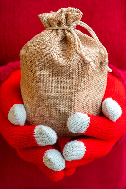 Mulher com um suéter quente e luvas de tricô vermelhas segurando uma sacola de presente de Natal