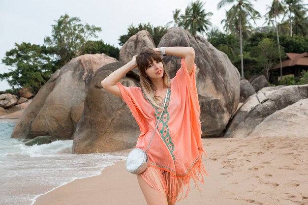 mulher com um vestido Boho caminhando na praia com pedras e palmeiras