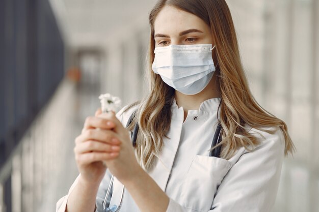 Mulher com uma máscara e uniforme segurando uma flor nas mãos