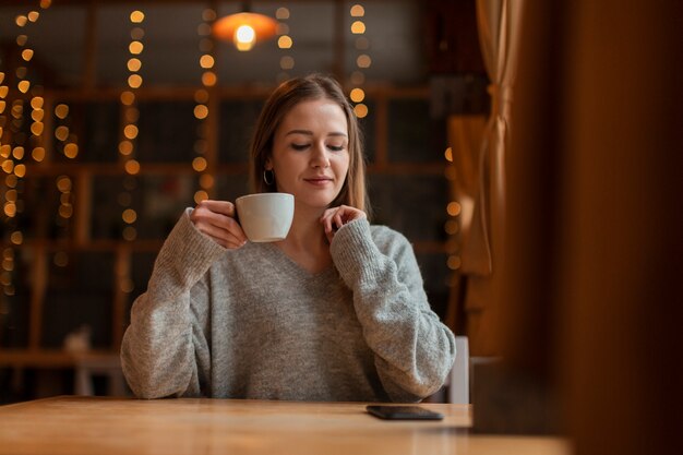 Mulher com uma xícara de café, olhando para o celular