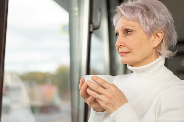 Mulher com uma xícara de café, olhando pela janela