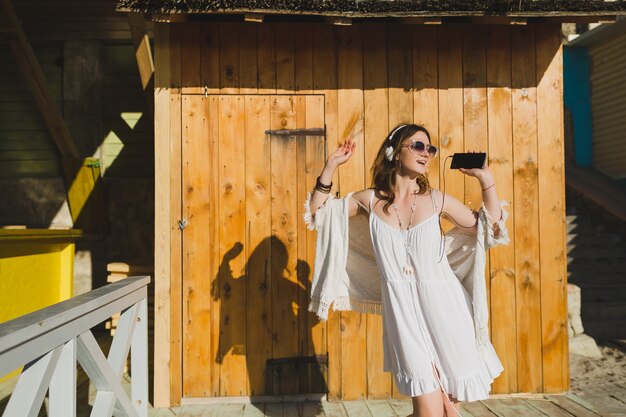 mulher com vestido branco de verão ouvindo música em fones de ouvido, dançando e se divertindo