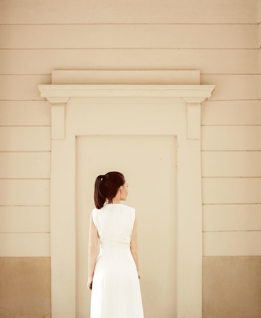 Foto grátis mulher com vestido branco perto da parede bege