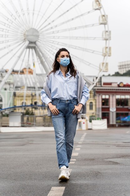 Mulher com vista frontal posando em um parque de diversões enquanto usava uma máscara médica