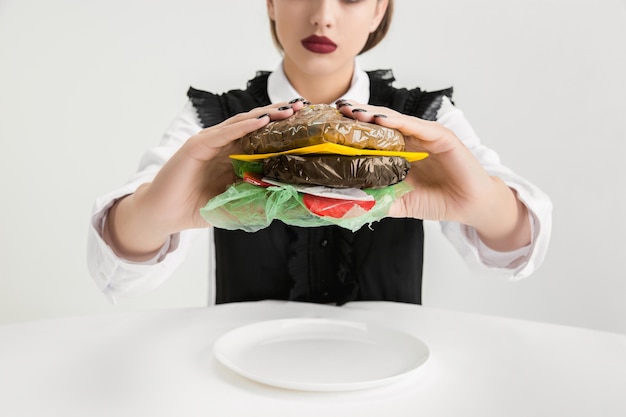 Mulher comendo hambúrguer feito de plástico, conceito ecológico.